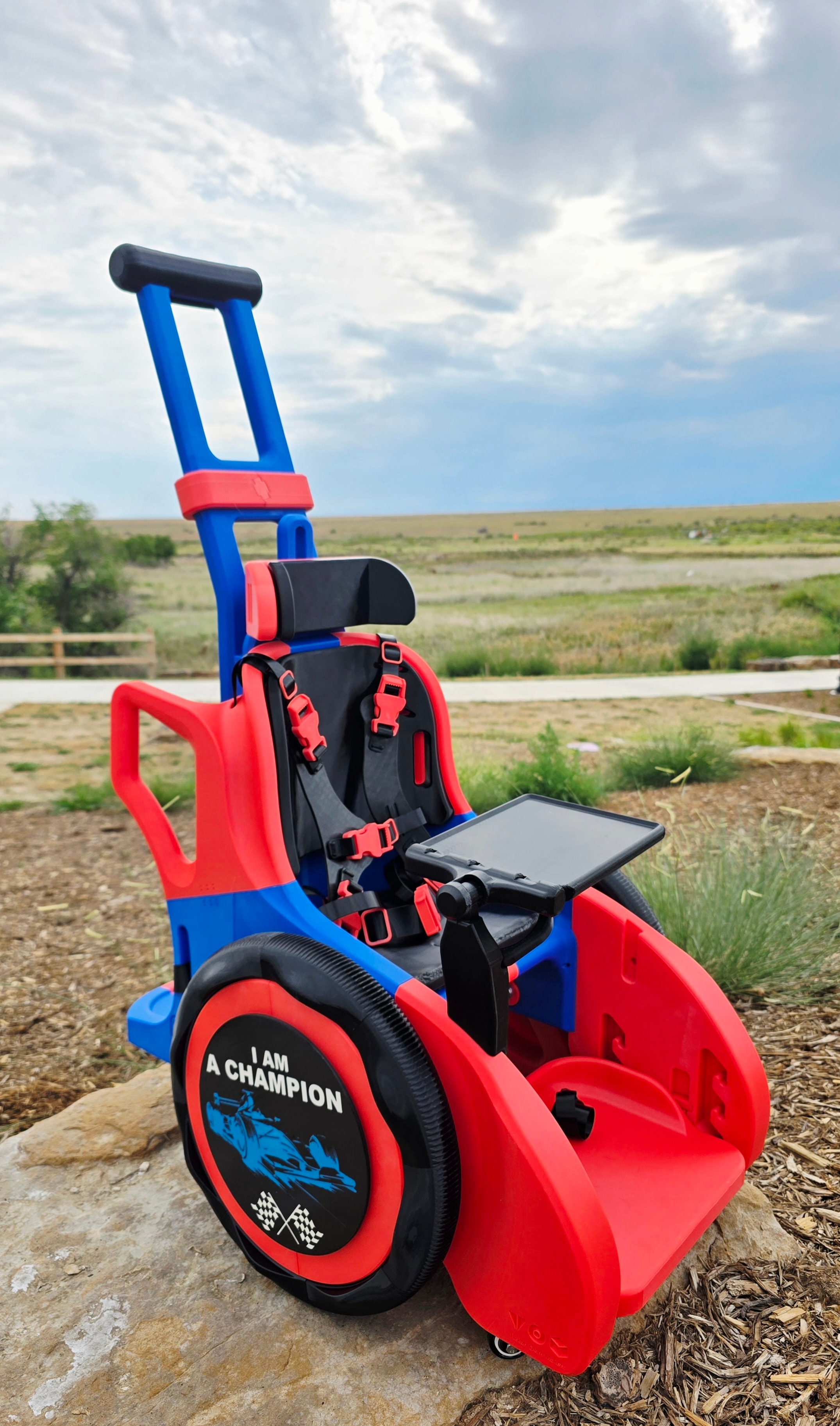 Red and blue 'I Am A Champion' children's mobility wheelchair outdoors